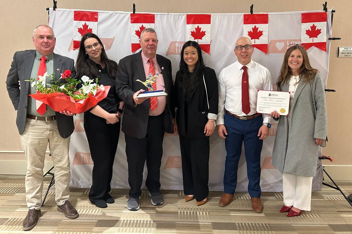 6 people stand in front of a backdrop featuring Canadian flags
